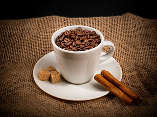 Ziarna kawy w białej filiżance na białym talerzyku z brązowym cukrem oraz cynamonem Postawione...
