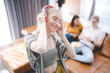 Happy young girl uses headphones to listen to music while relaxing at home with her family, and a gorgeous smiley woman enjoys her pastime and leisure time in the entertainment room. - obrazy, fototapety, plakaty