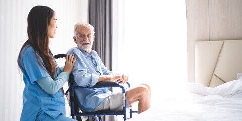 Full length portrait of Asian young female nurse assisting old senior man in wheelchair to looking at retirement home, carrying about disabled grey haired man in wheelchair, health insurance concept