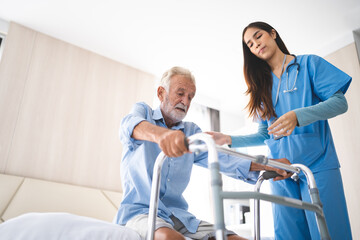 Obraz premium Portrait of Asian young nurse helping old elderly disable man grandfather to walk by using walker equipment in the bedroom. Senior patient of nursing home moving with walking frame and nurse support