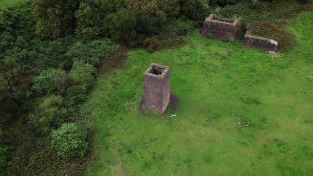 4K aerial footage of an old colliery chimney stack dated from 1865 in a field surrounded by bushes