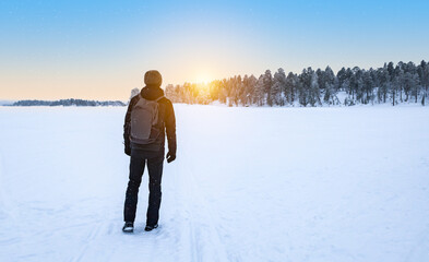 Male traveler with backpack walking in the snow enjoying the sunset. Lapland, Finland.