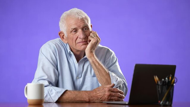 Portrait Of Happy Older Elderly Man Sitting At Desk With Laptop In Home Office. Confident 70s Businessman With Gray Hair Smiling Isolated On Solid Purple Background.