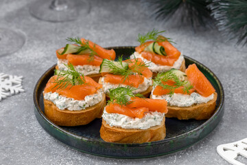 Salted salmon crostini with ribbon sliced cucumber, dill and herbed cream cheese (ricotta) on a plate. Gourmet snack. Close up, selective focus.