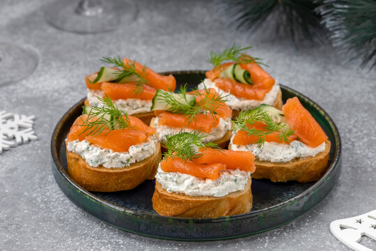 Salted salmon crostini with ribbon sliced cucumber, dill and herbed cream cheese (ricotta) on a plate. Gourmet snack. Close up, selective focus.
