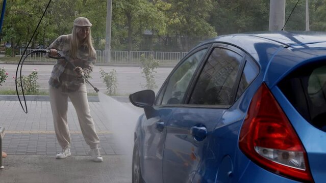 Woman washing a car in a self-service car wash station with wahing foam. Wash car self-service station