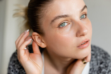 Portrait of young woman touching ear at home.