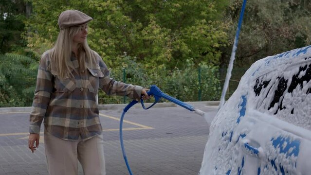 Woman washing a car in a self-service car wash station with wahing foam. Wash car self-service station
