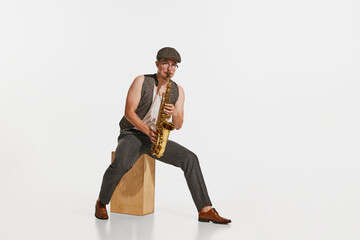 Young musician in retro style outfit playing saxophone isolated over white studio background. Concept of music, hobby, festival.
