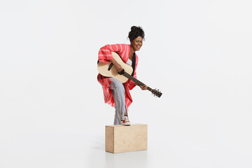 Melody. Stylish african woman wearing vintage style bright clothes playing guitar isolated on white...