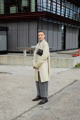 Stylish woman in trench coat looking at camera on urban street in Berlin.