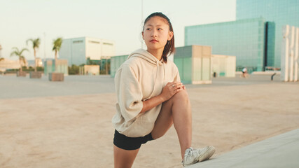 Asian girl in sportswear does workout, stretching and gymnastics on modern buildings background