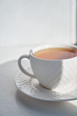 breakfast concept. white cup of tea couple coffee on white background, sunlight morning, hard shadows. side view, vertical photo, copy space, minimalism