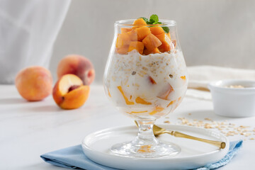 Peaches and Cream Overnight Oats. Healthy breakfast made with oats soaked for the night in milk or yogurt layered with cubes of fresh peaches, served in a clear glass.