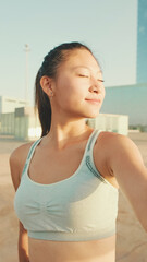 Fototapeta na wymiar Smiling asian girl in sports top makes selfie while standing on the embankment in the morning light