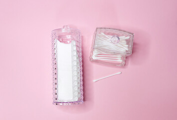White cotton square in a container for twitching and cotton buds on a light pink background. Cotton swab for ears, cosmetology, make-up and hygiene