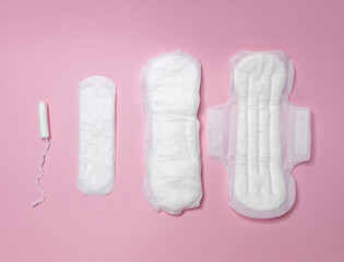White tampons and sanitary napkins lie on a light pink background. Menstrual cycle and pregnancy. Negative pregnancy test and contraceptives