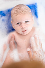 Baby bath time. Close-up detail view of mother bathing cute little peaceful baby in tub with water and bubbles lather.