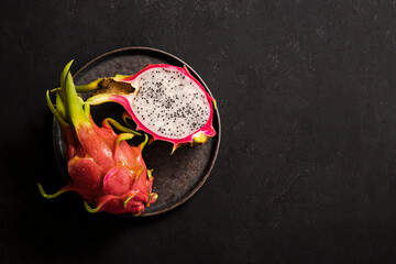 Tropical pitaya fruit on a black plate and black background. Background splash with tropical fruits, copy space for text