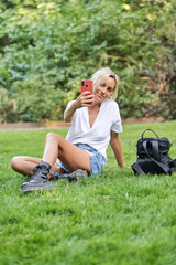 Young woman taking selfies with a mobile phone while sitting on grass outdoors. Technology concept.