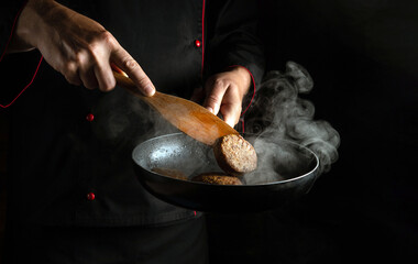 Professional chef frying burger cutlets in a frying pan. Close-up of a cook hands with a hot pan in...