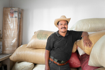 Portrait of an Hispanic farmer smiling next to his coffee sacks in the warehouse