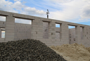 Crushed stones and sand in front of in front of a foam concrete bricks cottage under construction

