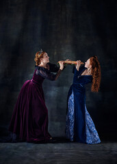 Portrait of two beautiful women in image of queens fighting for giant sandwich isolated over dark background