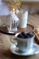 Vintage tea set filled with blueberries, blackberries and starwberries, open book, reading glasses and decorative candles on the table. Selective focus.