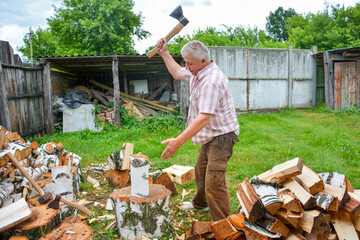 On a sunny summer day, a man is chopping firewood in the yard.