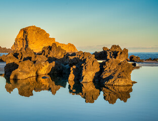 Rocks reflections at sunset. Natural lava pools and ocean in the background