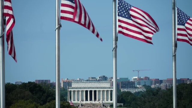 Distant closeup view of Lincoln Memorial Arlington, VA, and airplane landing through the flags waving in the wind at the Washington Monument in Washington DC.
