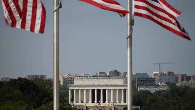 Distant closeup view of Lincoln Memorial and Arlington, VA through the flags waving in the wind at the Washington Monument in Washington DC.