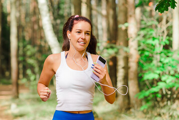 Young pretty woman running in the park at summer morning.The girl is listening to music while running.Sport and health nature concept.Close-up.