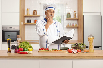 Mature male chef holding a cook book and thinking in a kitchen