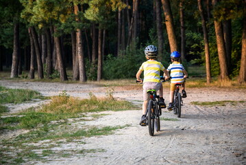 Fototapeta premium Family in the park on bicycles. two sibling brothers kids boys compete in riding. view from back
