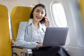 Young Asian business woman talking on smartphone, businesswoman working while flying at plane, Young woman using the internet at airplane, Air travel, long flight.