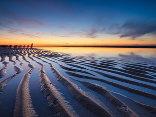 A seascape during sunset. Lines of sand on the seashore. Bright sky during sunset. A sandy beach at low tide. Travel image. Photography for design.