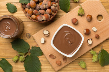 Hazelnut cream with nuts and green leaves on wooden background, top view