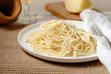 Cacio e Pepe - Italian pasta with grated Pecorino Romano cheese and black pepper, together with spaghetti in a white plate on wooden background. Close up,  flat lay, copy space.