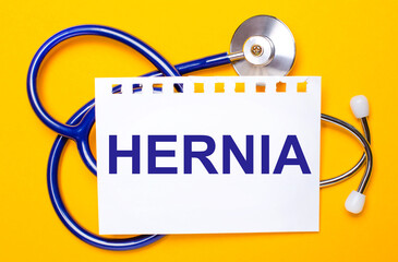 On a bright yellow background, a blue stethoscope and a sheet of paper with the text HERNIA....
