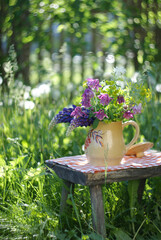 Still life on a sunlit lawn with a bunch of colorful summer flowers in a jug on a small wooden bench in rustic style