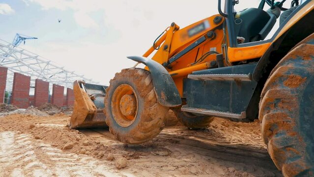 A large yellow excavator is driving on a construction site. Excavator wheels close up