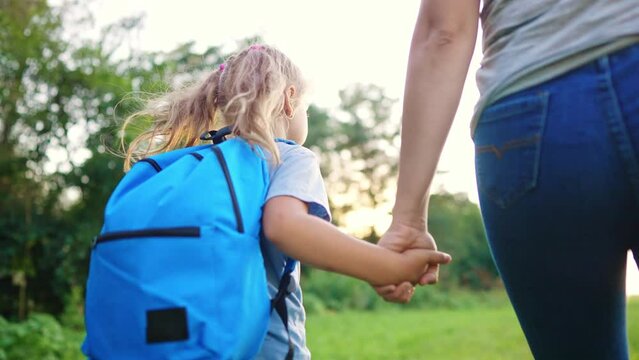 mother and daughter go to school. happy family education concept. schoolgirl with mom and daughter go hand in hand to school along path in the park. little girl with.time to study briefcase