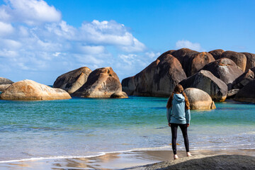 girl in ponytails standing on the beach with massive rocks in the background, elephant rocks in...