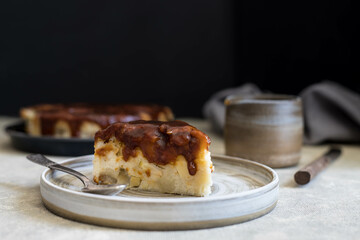 a piece of apple pie with caramel on a light handmade ceramic plate.