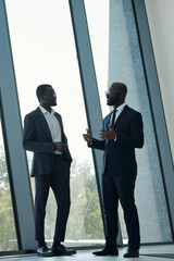 Young confident African American male employee in elegant suit explaining something to colleague at meeting in office center