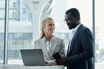 Happy young businesswoman looking at colleague while explaining him points of presentation of new business project at meeting