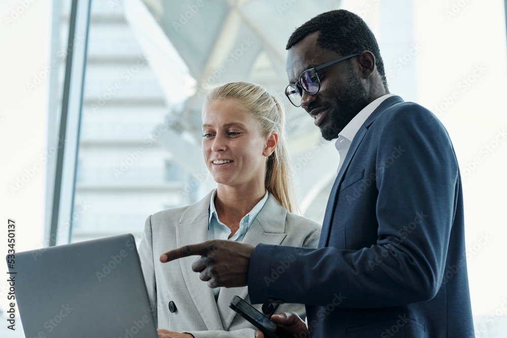 Poster young confident businessman in formalwear pointing at online data on laptop screen while explaining 
