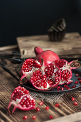 beautiful pomegranate fruits with pits on a metal plate on a wooden table in a dark key in rustic style